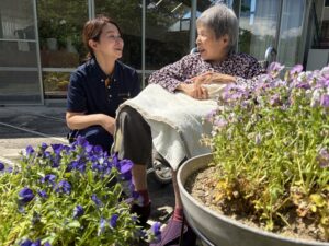 花壇の前で利用者の方と笑顔の特養介護員 Sさんの画像