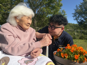 鉢の花見ながら利用者の方と笑顔のSさんの画像