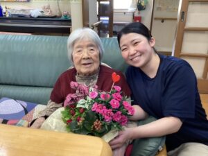 利用者の方と花を持ちながら笑顔のMさんの画像