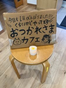 イスに置かれたお疲れカフェの手書きの看板の画像